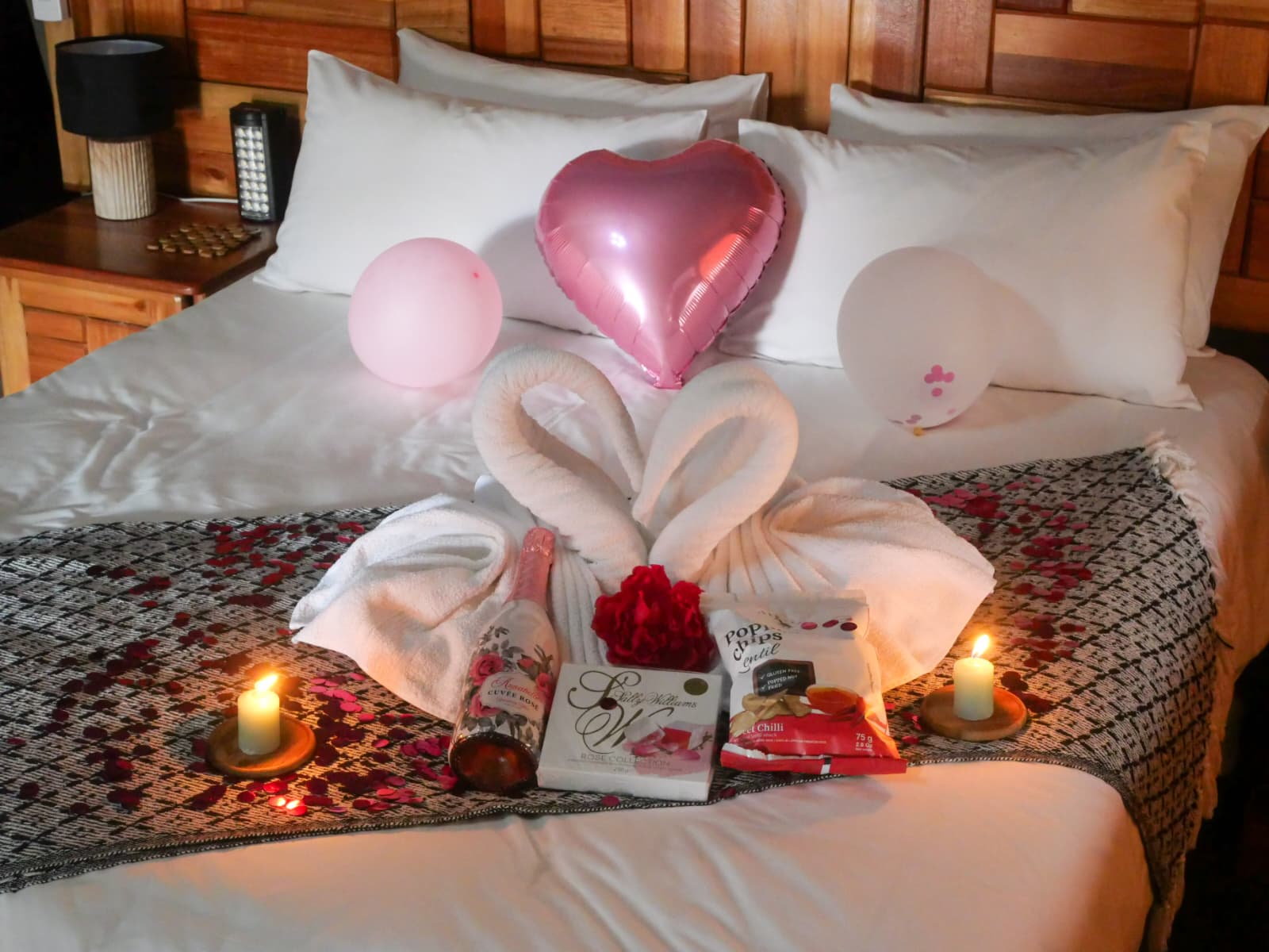 Bed decorated with towel swans, balloons and candles for a romantic surprise
